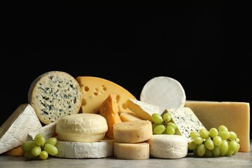 Different types of cheese and grapes on grey table against black background