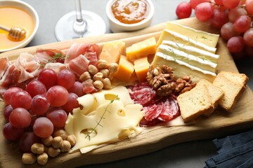 Different types of cut cheese and other snacks on gray table, closeup