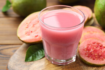 Tasty guava juice in glass, leaf and fruits on wooden table, closeup