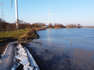 Ice on the edge of the lake in winter. Freezing temperature below 0, causing the frozen water at the edge of the beach to be spicy. A deserted nature area with windmills and a beach.