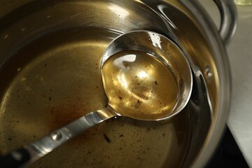 Used cooking oil and ladle in saucepan on stove, closeup