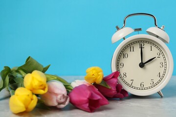 Spring time. Alarm clock and beautiful tulips on grey marble table against light blue background