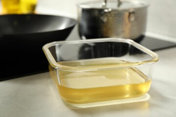 Used cooking oil in glass container on white marble countertop, closeup