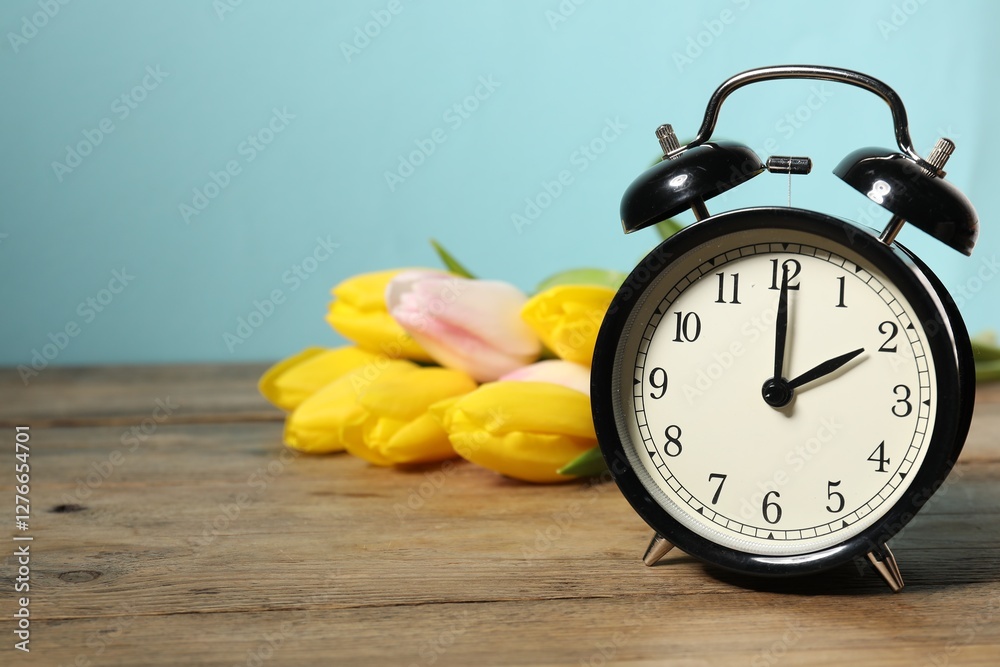 Poster spring time. alarm clock and beautiful tulips on wooden table against light blue background, space f