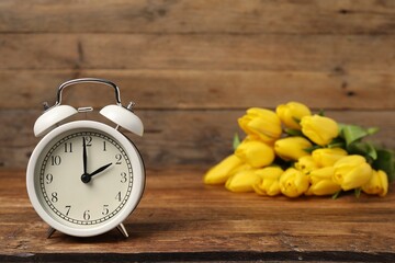 Spring time. Alarm clock and beautiful tulips on wooden table