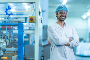 A confident food processing supervisor in protective gear, standing with arms crossed next to machinery in a factory, symbolizing leadership, quality assurance, and operational safety.
