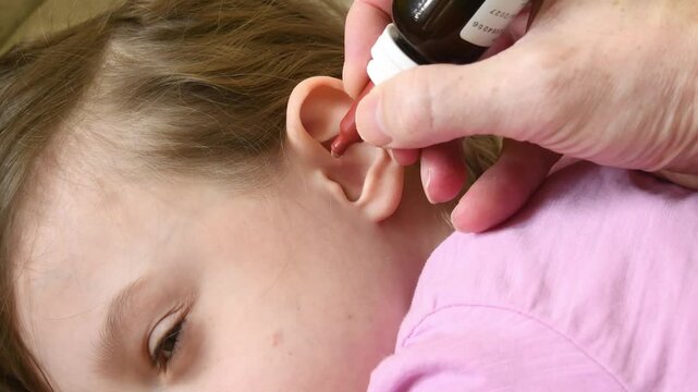 Close-up of child ear as adult applies ear drops from bottle. Pediatric ear infection treatment, medical care, home health therapy.