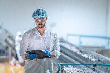 A factory worker in protective gear conducting a checklist inspection in a production facility.