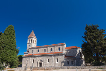 Fototapeta premium Stone Church With Bell Tower Surrounded by Green Trees Against a Blue Sky, Grohote, Solta