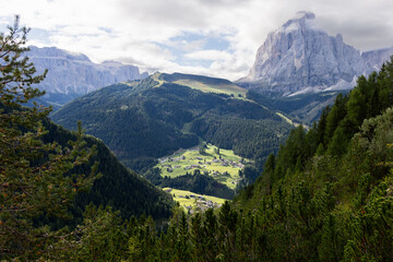 Val Gardena stretches below the towering Sassopiato, featuring alpine meadows, vibrant forests, and charming villages surrounded by rugged peaks
