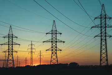 A group of power lines are silhouetted against a beautiful sunset
