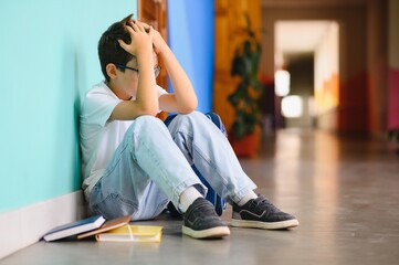 Little boy sitting alone on floor after suffering an act of bullying. Sad young schoolboy sitting...