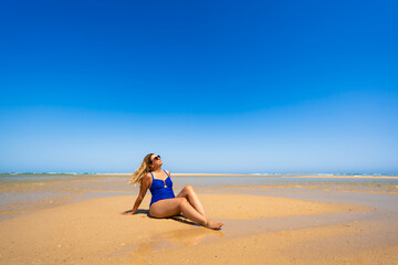 Summer holidays on Armona island in Portugal. Beautiful middle-aged woman sunbathing on sandy idyllic beach