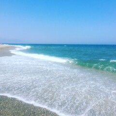 Sandy beach with gentle waves rolling in. Clear blue sky above. Coastal scene with foamy water and natural light. Peaceful ocean landscape. Travel and nature
