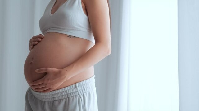 Young happy pregnant woman posing in studio with white curtains in background