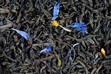 dry black tea leaves with flower petals scattered on the surface