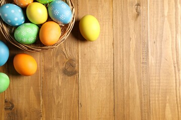 Beautiful decorated Easter eggs and wicker bowl on wooden table, flat lay. Space for text