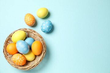 Beautiful decorated Easter eggs and wicker bowl on light blue background, flat lay. Space for text
