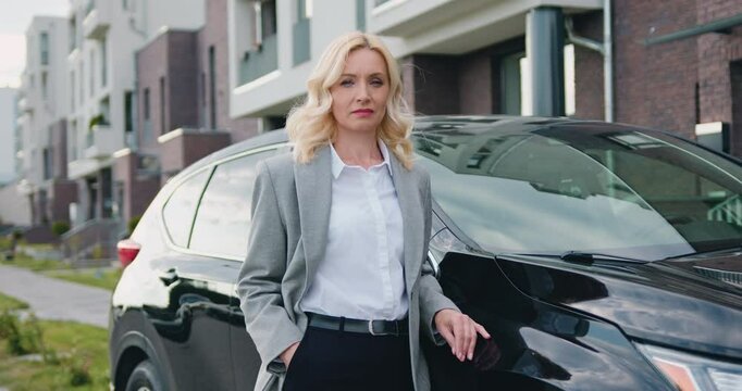 Portrait of businesswoman in official clothes outside when standing beside black car on parking near modern building. Outdoors.