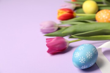 Easter eggs, beautiful tulips and ribbon on lilac background, closeup. Space for text