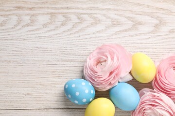 Easter eggs and beautiful flowers on wooden background, flat lay. Space for text