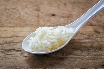 Cooked white rice or steamed rice in a white spoon on wooden background