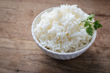 Cooked white rice or steamed rice in a white bowl on wooden background