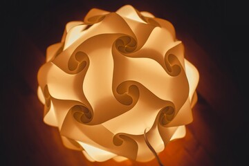 Warm glowing spherical lamp with intricate curved design, creating a cozy and modern atmosphere. Soft light and abstract shapes enhance the artistic aesthetic