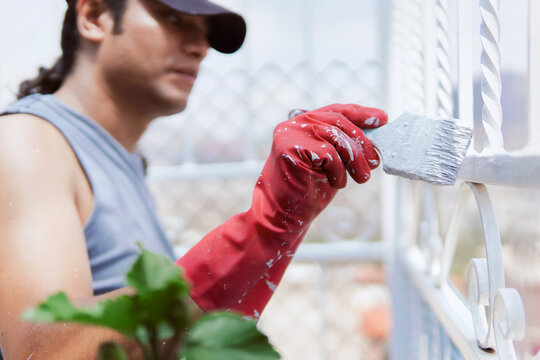 Latino worker of Mexican origin carrying out his work, painting a fence with white paint, happy, relaxed and dirty