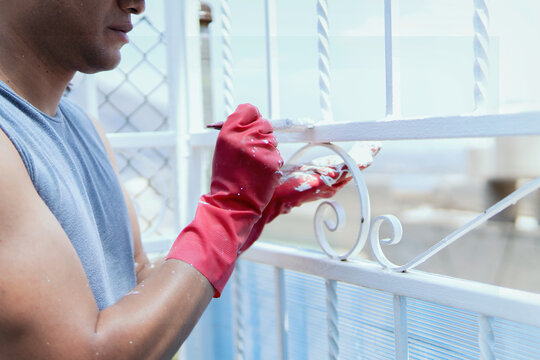 Latino worker of Mexican origin carrying out his work, painting a fence with white paint, happy, relaxed and dirty