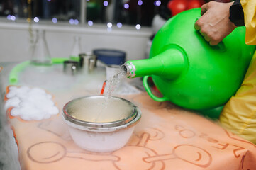 An animator pours liquid nitrogen from a large tank into a glass bowl, conducting a chemical...