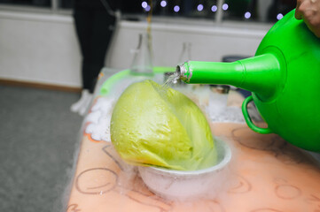 An animator pours liquid nitrogen from a large reservoir into a glass bowl with a balloon,...