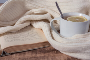 Reading a book with cup of hot tea with lemon. Still life with warm scarf, cup and old book on a wooden table.