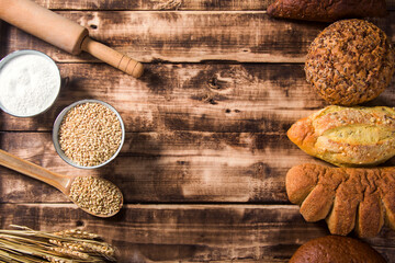 bread with wheat ears and a bowl of flour on a dark board, top view