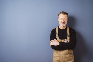 Smiling senior man in work overalls with arms crossed