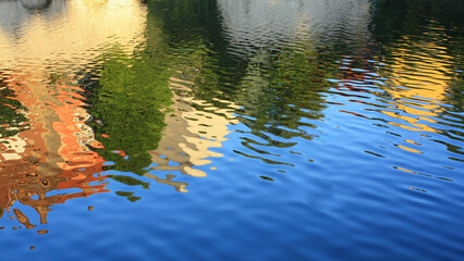 Colorful reflections of buildings and trees on rippling water

