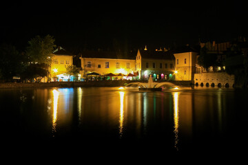 Nighttime cityscape with illuminated fountain and reflections on water
