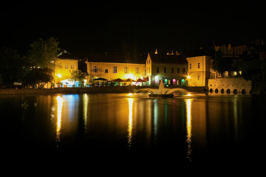 Nighttime cityscape with illuminated fountain and reflections on water
