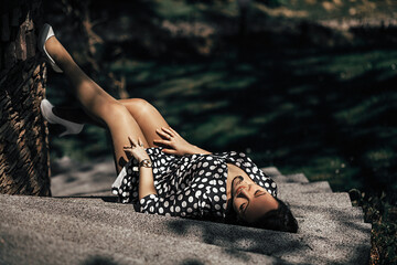 A woman lies on a stone surface, wearing a polka dot dress. She leaned back relaxed, closing her eyes, and seemed to be enjoying the sun's rays.