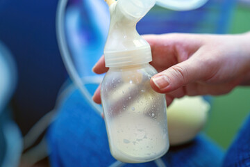 woman's hand holds a plastic bottle containing a small amount of breast milk from an automatic...