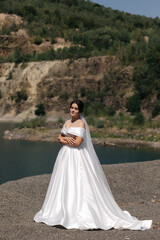the bride stands outside against the backdrop of nature, trees and rocky terrain are visible.