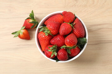 Delicious fresh red strawberries in a bowl on a wooden background