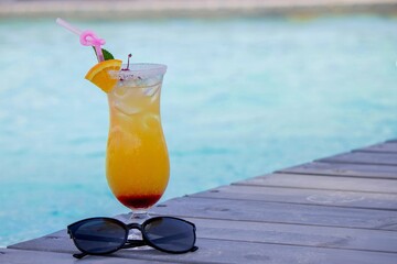 A nice cocktail, hat and sunglasses by the pool