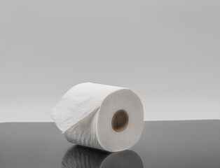 A solitary roll of white paper sits on a glossy black surface, showcasing its smooth texture. The backdrop is neutral, emphasizing the roll's simplicity and function in daily life.