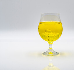 A glass containing a vibrant yellow beverage sits on a smooth surface. Ice cubes rest inside the drink, creating a refreshing appearance, perfect for a warm day.
