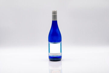 A striking blue glass bottle stands upright against a smooth, light background. The bottle features a blank white label, making it suitable for various beverages, enhancing its appeal.