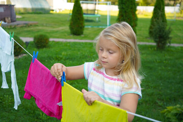 Sunlight filters through the trees as a six-year-old girl happily hangs laundry, her braids swaying with each careful movement.