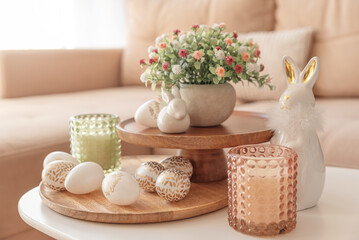 Easter eggs, candles and white ceramic rabbits on wooden table in interior of living room