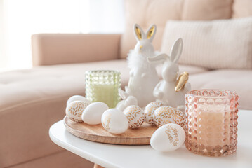 Easter eggs, candles and white ceramic rabbits on wooden table in interior of living room