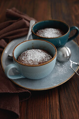 Two chocolate mug cake under sugar icing on dark wooden table. Easy homemade dessert. Mugcake from microwave